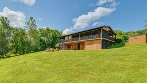 A two-story house with a balcony on the second floor, surrounded by a grassy lawn and trees.