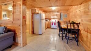 A wooden interior with a kitchen area featuring a refrigerator, stove, and dining table with chairs.