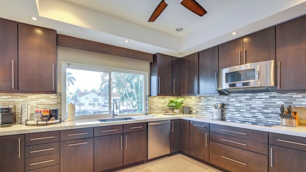 A modern kitchen with dark wood cabinets, a stainless steel microwave, and a large window providing natural light. - Canal Access & Pool: Lighthouse Point Getaway! (Pompano Beach)