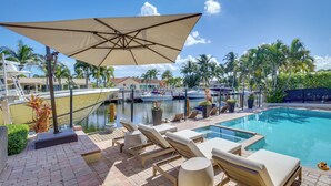 A poolside area with lounge chairs, a large umbrella, and a view of the marina with boats. - Canal Access & Pool: Lighthouse Point Getaway! (Pompano Beach)