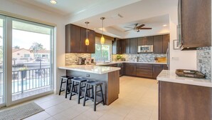 A modern kitchen with dark wood cabinets, a large island with stools, a microwave, and a ceiling fan. - Canal Access & Pool: Lighthouse Point Getaway! (Pompano Beach)