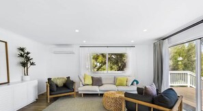 Een moderne woonkamer met een bank, twee fauteuils, een salontafel en een groot raam met gordijnen.