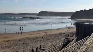 Une plage où l’on voit des gens se promener et se tenir debout, une promenade en bois et une falaise en arrière-plan.