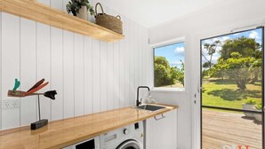 Une cuisine moderne avec un plan de travail en bois, un lave-linge et une fenêtre donnant sur un paysage verdoyant.