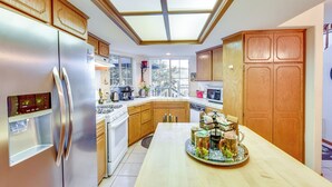 Una cucina moderna con frigorifero in acciaio inossidabile, pensili in legno, un lucernario e una penisola colazione con frutta esposta.