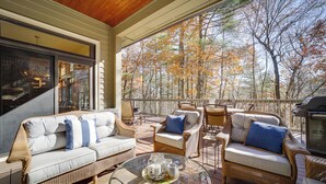 A covered outdoor seating area with wicker furniture and a glass table, overlooking a forested area. - 5 Mi to Sapphire Valley Skiing: Serene Family Home (Sapphire)