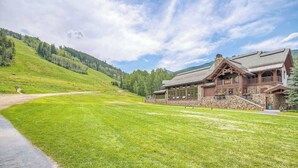 Un chalet doté d’une façade en pierre, de grandes fenêtres et d’un balcon donnant sur un paysage verdoyant, avec une montagne en arrière-plan.