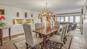 Un coin repas comprenant une grande table en bois, six chaises rembourrées, un tapis à motifs et un lustre décoratif.