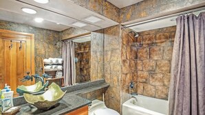 Une salle de bain avec un pare-baignoire en pierre, une baignoire sur pieds, un lavabo doté d’un design original et un meuble-vasque en bois.