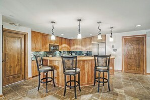 A kitchen with wooden cabinets, a marble countertop, and three bar stools. - Ski-In & Ski-Out Alpine Enchantment | Beaver Creek (Beaver Creek)