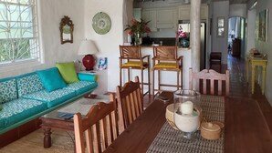 Een woonkamer met een bank, stoelen, een salontafel en een keuken op de achtergrond.
