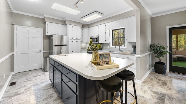 A modern kitchen with white cabinetry, a large island, and a bar stool. - NEW - Modern Cabin Oasis - 2 Acre Retreat! (Apex)
