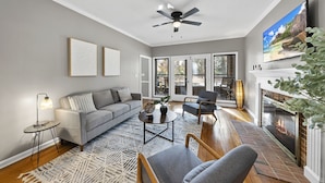 A modern living room with a grey sofa, a coffee table, and a fireplace. - NEW - Modern Cabin Oasis - 2 Acre Retreat! (Apex)