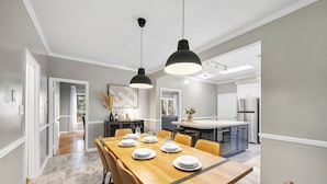 A modern dining area with a wooden table set for six, a kitchen in the background, and pendant lighting. - NEW - Modern Cabin Oasis - 2 Acre Retreat! (Apex)