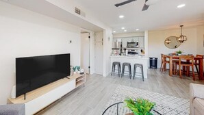Ein modernes Wohnzimmer mit Flachbildfernseher, Deckenventilator und Essbereich mit Holztisch und Stühlen.