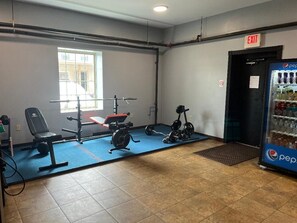 A gym with exercise equipment, a window, an exit sign, and a Pepsi refrigerator.