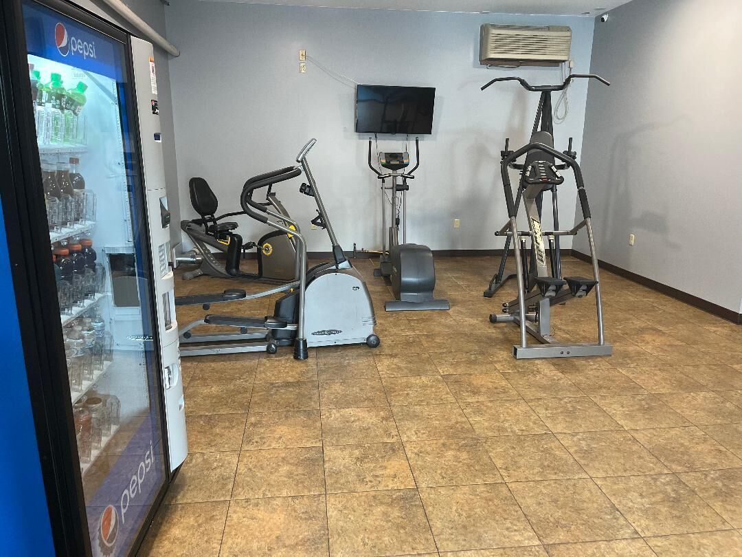 Ein Fitnessbereich mit Trainingsgeräten, einem Fernseher und einem Kühlschrank für Pepsi.
