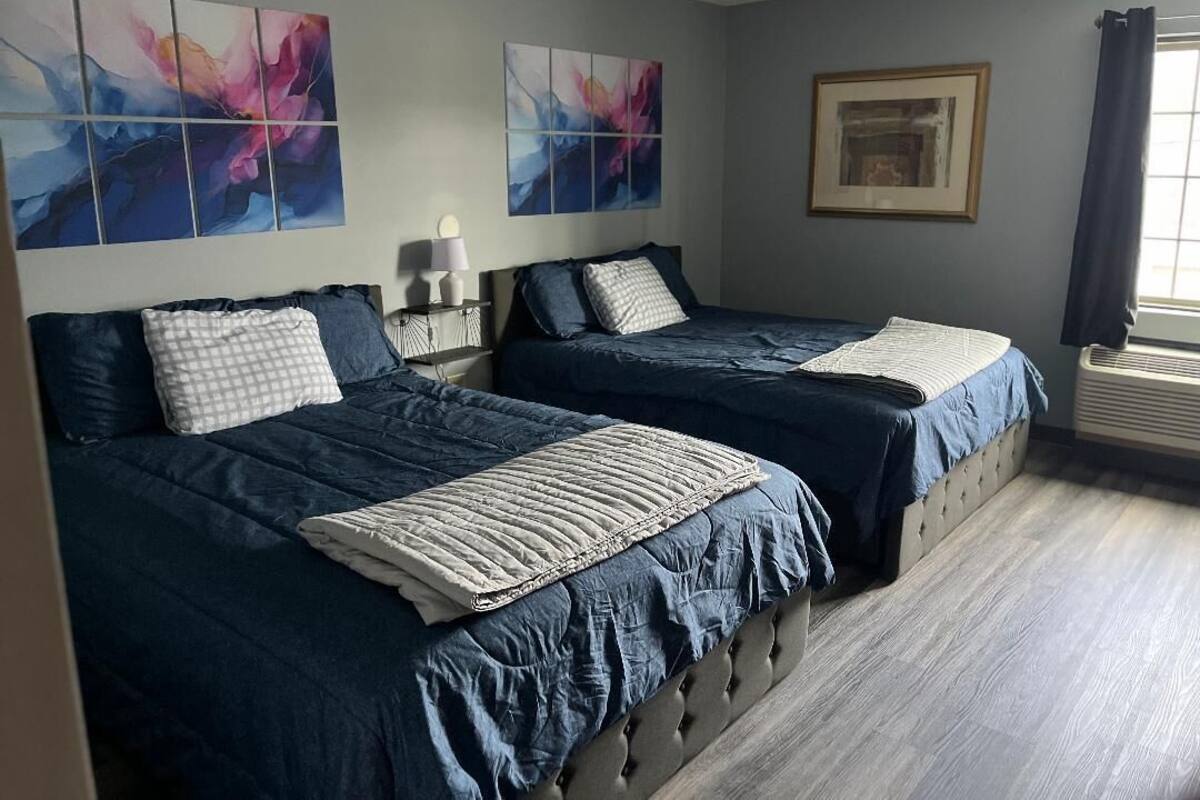 A bedroom with two beds, a bedside table, a lamp, and abstract wall art.