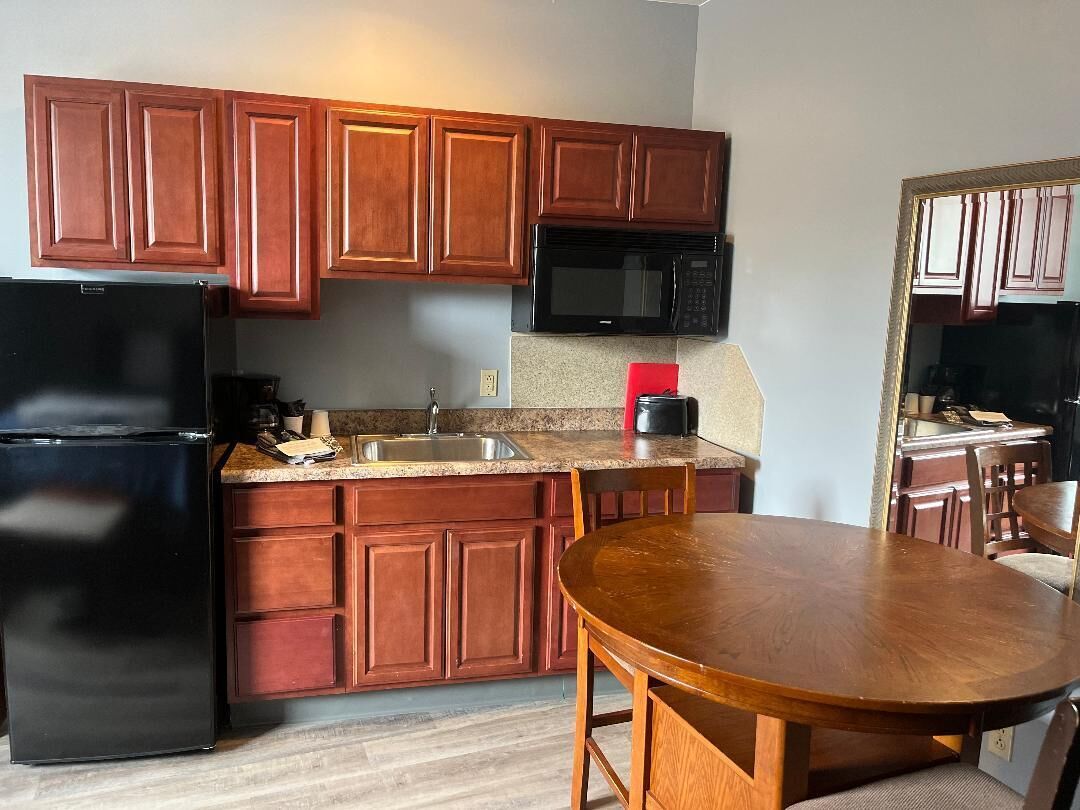 A kitchen with wooden cabinets, a black refrigerator, a microwave, a sink, and a dining table with chairs.