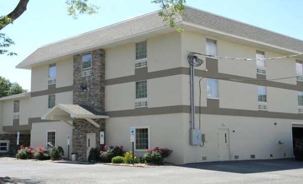 A multi-story hotel with a stone facade, multiple windows, and a parking area with flowers.