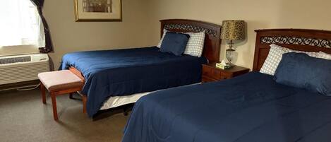 A hotel room with two beds, a bench, a bedside table with a lamp, and a framed picture on the wall.