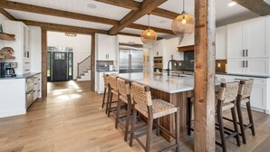 A spacious kitchen with a large island, wooden beams, white cabinetry, and a stainless steel refrigerator. - Custom built Adirondack style home sleeps 16 in 6 bedrooms (Moultonborough)