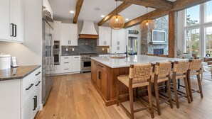 A modern kitchen with white cabinets, a wooden island, and a stone fireplace. - Custom built Adirondack style home sleeps 16 in 6 bedrooms (Moultonborough)