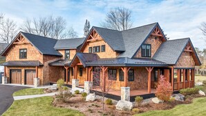 A multi-story log cabin with a covered porch, a garage, and a landscaped front yard with rocks and shrubs. - Custom built Adirondack style home sleeps 16 in 6 bedrooms (Moultonborough)