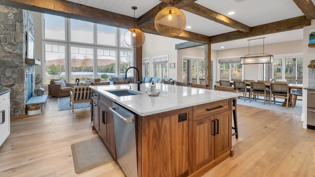 A spacious kitchen with a large island, wooden cabinets, and a stone accent wall. - Custom built Adirondack style home sleeps 16 in 6 bedrooms (Moultonborough)