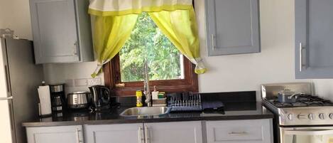 A kitchen with grey cabinets, a stove, a sink, and a window with a yellow curtain.