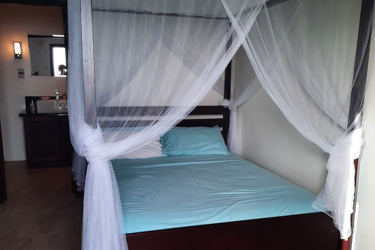 Un lit à baldaquin avec des rideaux légers, un matelas bleu clair et un cadre en bois foncé.
