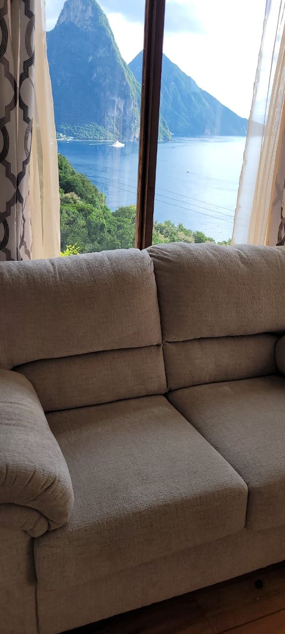 Un sofà beix a una habitació amb un finestral gran que dona a un paisatge de muntanyes i un cos d'aigua.
