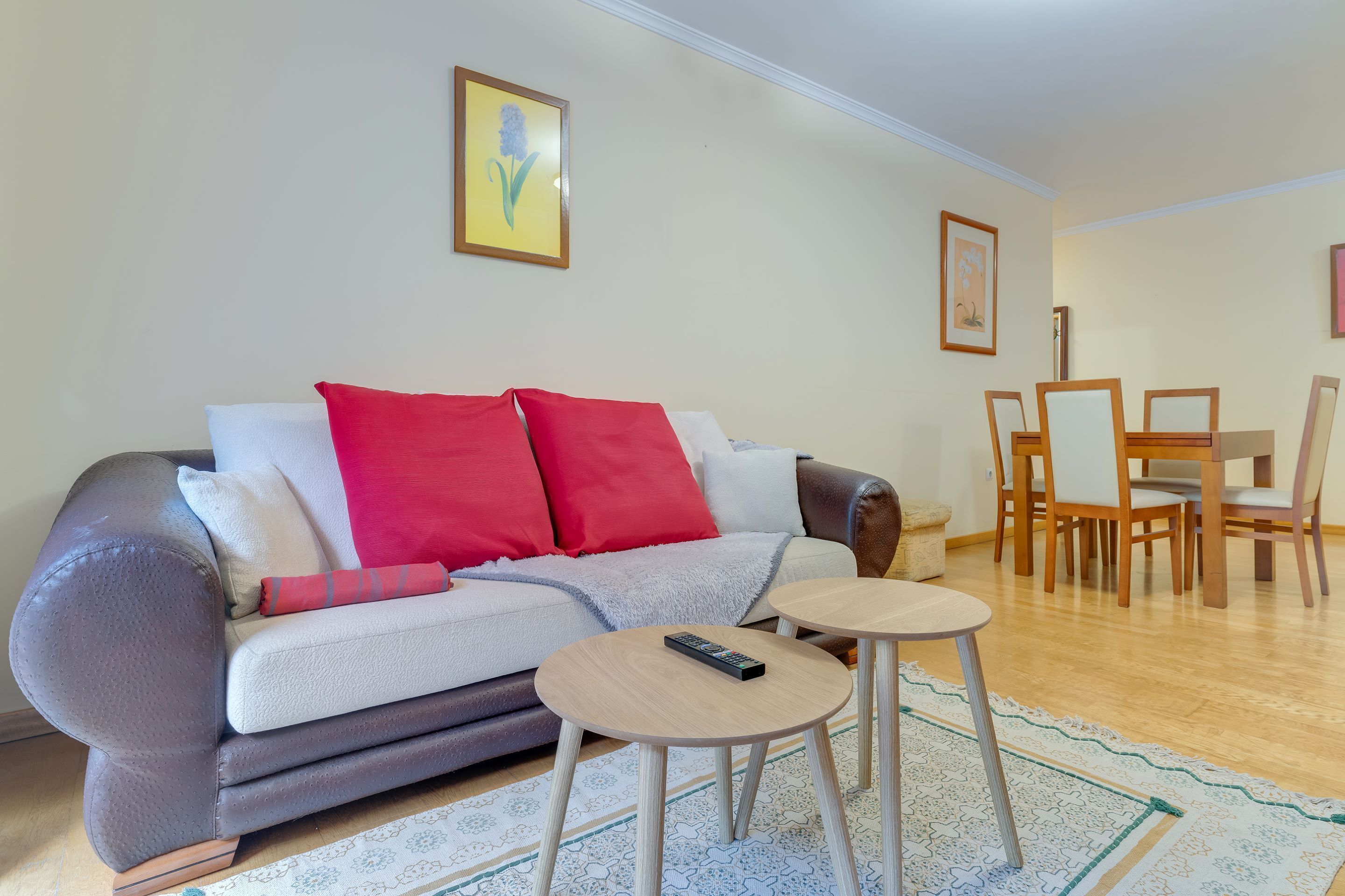 A living room with a sofa, two small tables, and a dining area with chairs and a table.