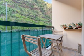 A balcony with a wooden table and chairs, a green mesh fence, and potted plants. - Isabel Apartment (Ribeira Brava)