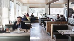 Een restaurant met houten zithoeken en tafels, grote ramen en een informele sfeer.