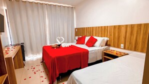 A hotel room with two beds, a wooden headboard, a desk with a lamp, and a window with curtains.
