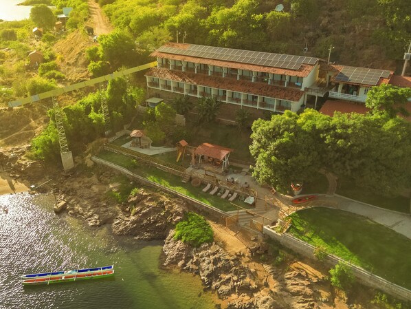 A large building with a tiled roof, a swimming pool, and a dock with a boat. - Pousada Porto de Piranhas (Piranhas)