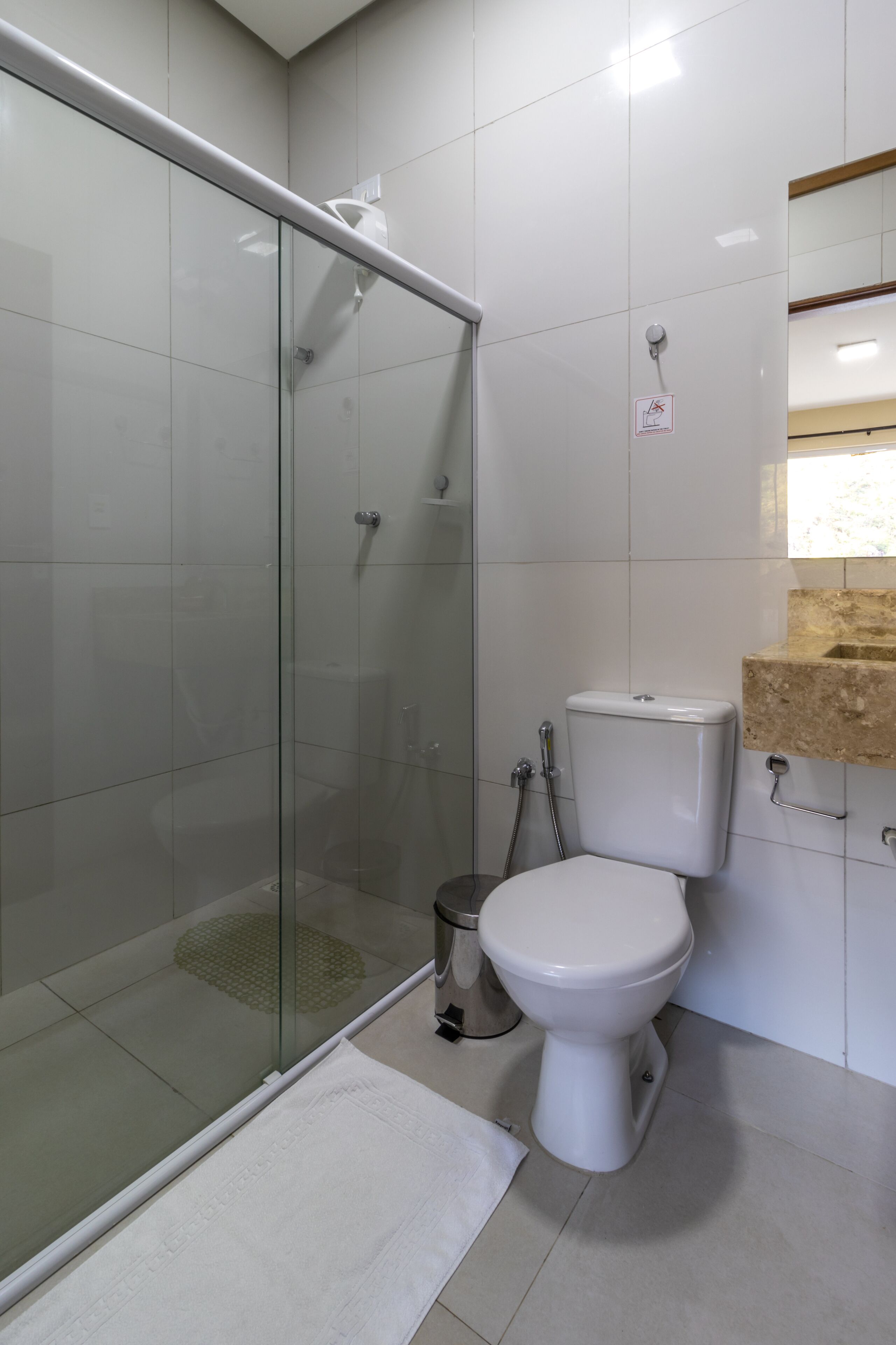 Un bagno con doccia vetro-muraria, un water e un lavandino con piano d'appoggio color beige.
