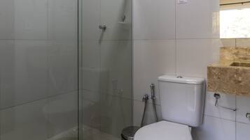 Un bagno con doccia vetro-muraria, un water e un lavandino con piano d'appoggio color beige.