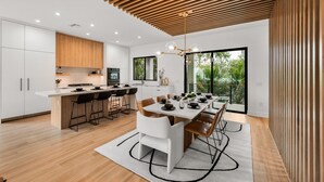 A modern kitchen with a central island, bar stools, and a dining area with a large table and chairs. - Brand New home with Incredible Rooftop Deck and Pool! - Just Breathe (Anna Maria)