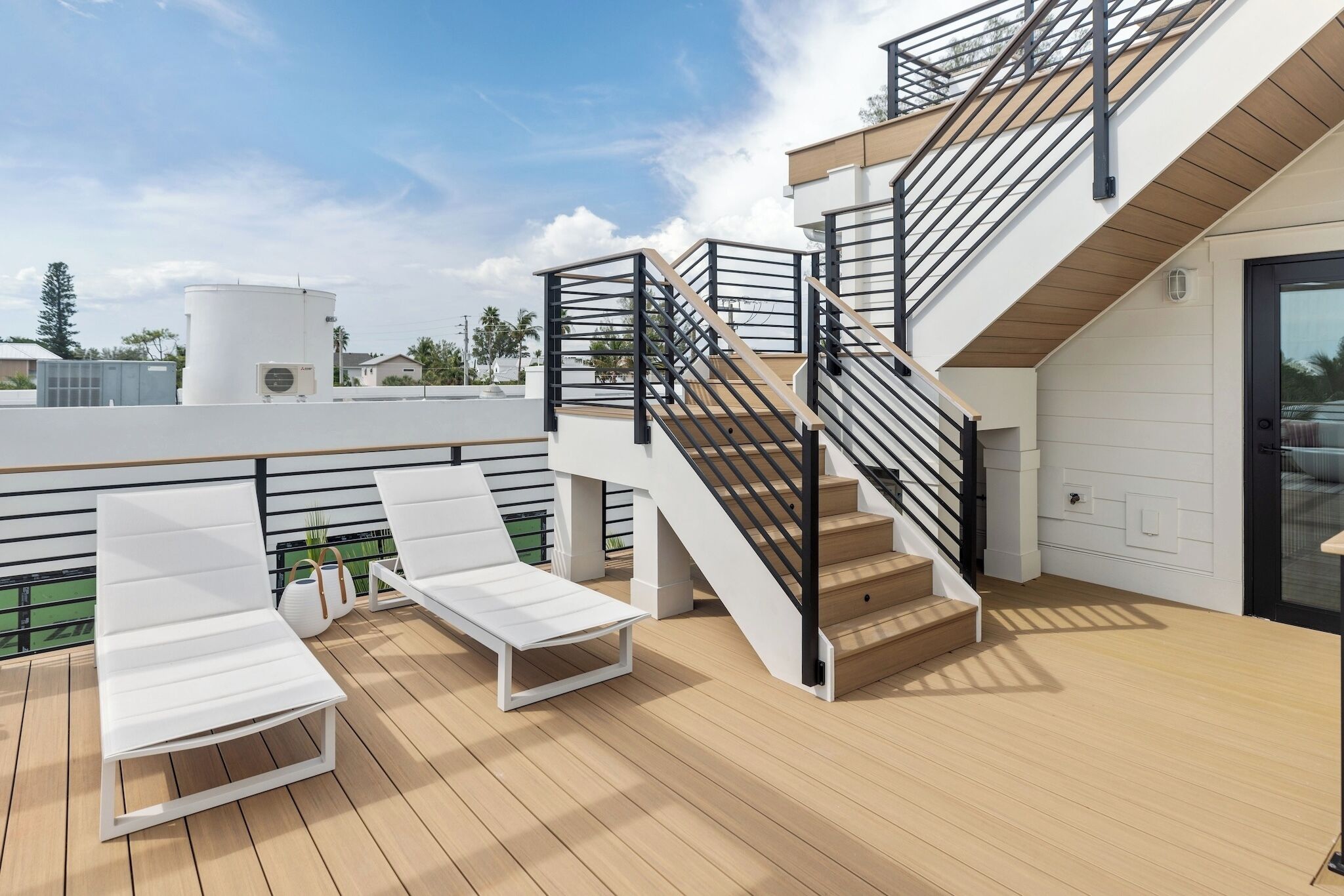A rooftop deck with two white lounge chairs, a staircase, and a white cylindrical tank.