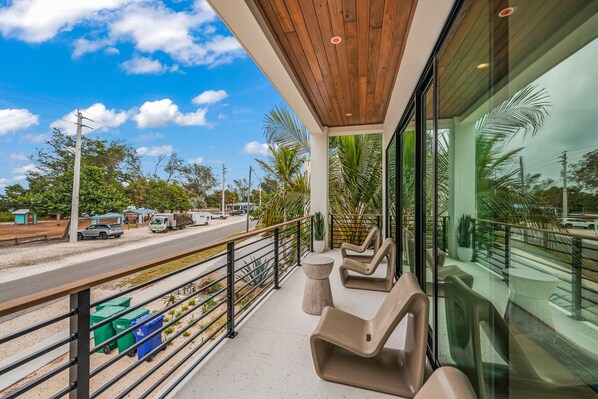 A modern outdoor seating area with a wooden ceiling and glass walls, overlooking a road with vehicles and greenery.