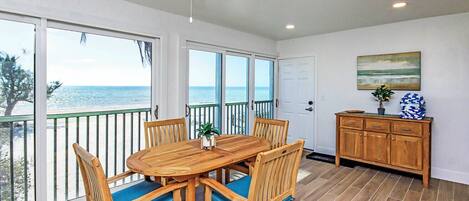 A dining area with a wooden table and chairs, a view of the ocean, and a wooden cabinet with decorative items.