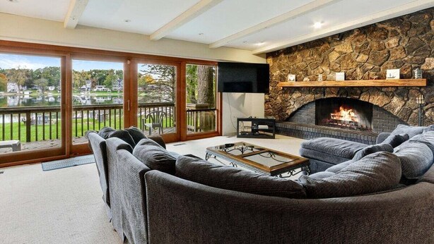 A cozy living room with a stone fireplace, large windows, and a view of a lake. - The Lake House on Powers |Grassy Frontage |Lakeside Deck |Rec Room w/Pool Table & Bar |Fire Pit (Genoa City)