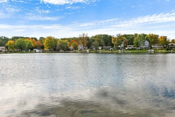Vista de un lago con casas y árboles en tonos otoñales.