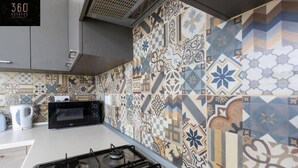 A modern kitchen with a gas stove, a microwave, and a kettle. The backsplash features a variety of geometric and floral tile patterns. - Central & Spacious Penthouse w/ 1BR + City View (L-Imsida)