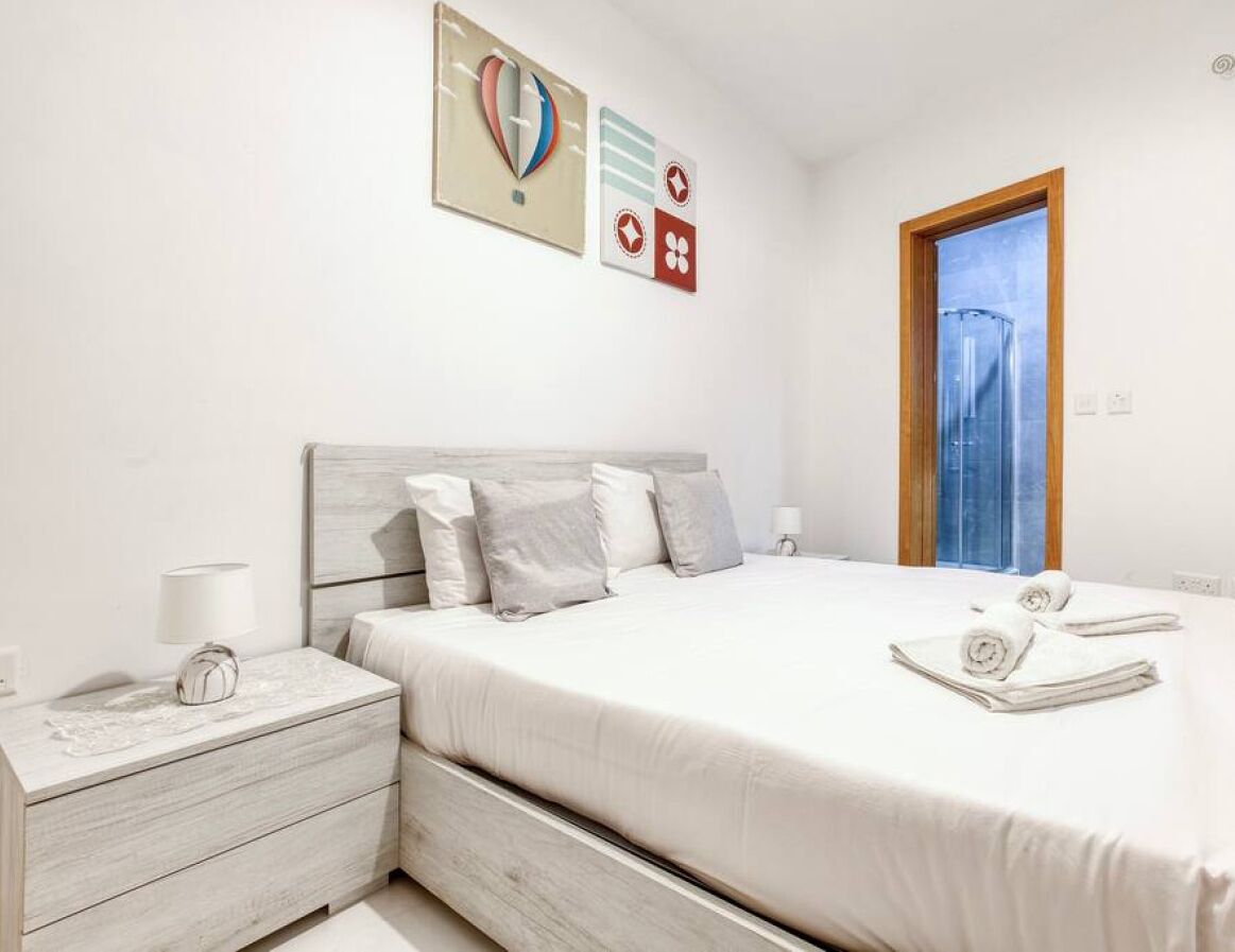 Une chambre à coucher bien rangée, avec un lit, des tables de chevet, une lampe et une fenêtre.