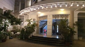 Entrada de hotel con fachada curva, plantas en macetas y una escalera que lleva a la recepción.