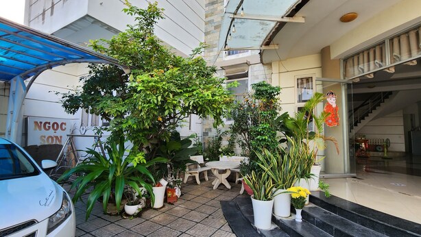 Entrada de hotel con un área de estar al aire libre cubierta, plantas en macetas y una escalera que da al interior.