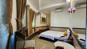 Habitación de hotel con dos camas, una mesita, sillas, un espejo y un ventilador de pared.
